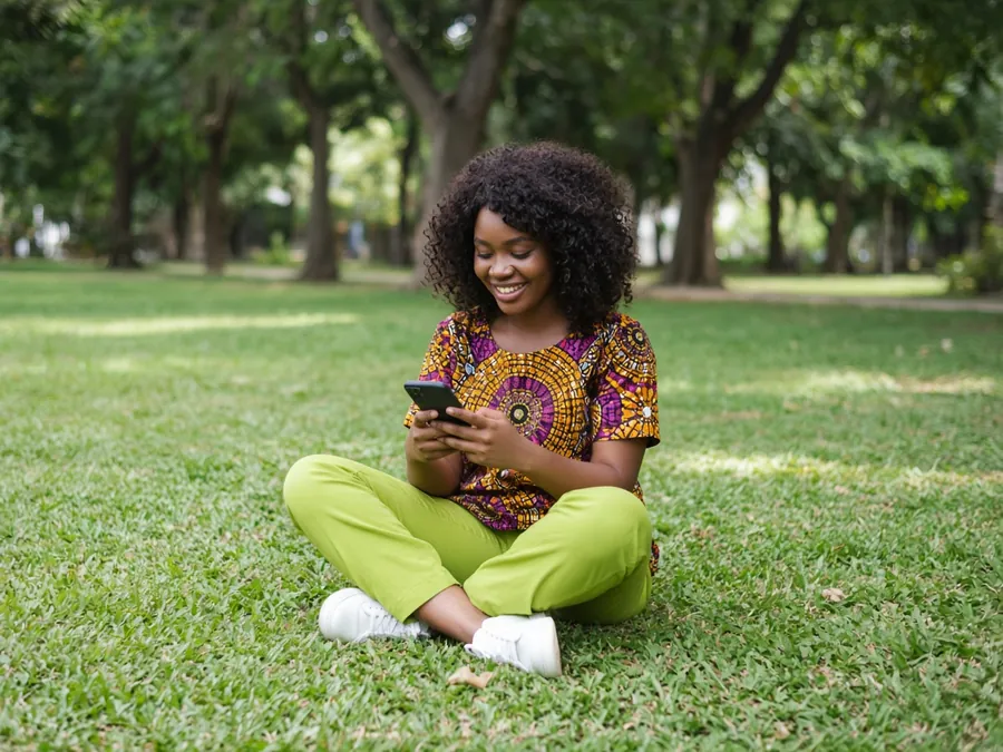 Woman sitting on the grass, smiling at her phone
